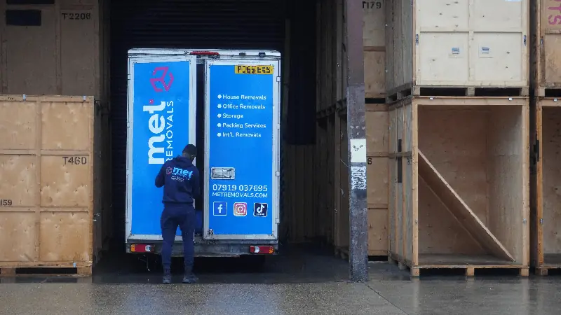 MET Removals porter opening the back of a MET Removals van between stacked wooden storage containers, storage for Chigwell moves