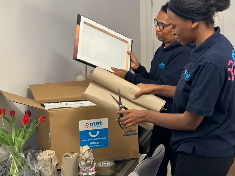 Two MET Removals packers wrapping a framed picture beside a branded box, packing services in Crouch End
