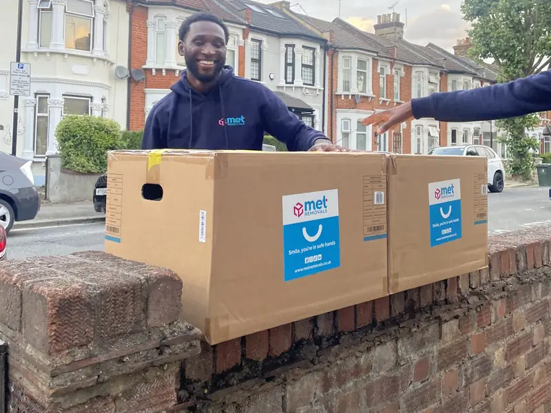 MET Removals mover lifting packed boxes over a garden wall on a terraced street, house removals in Crouch End